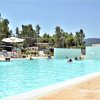 Una piscina all'aperto con bagnanti, circondata da verde e ombrelloni.